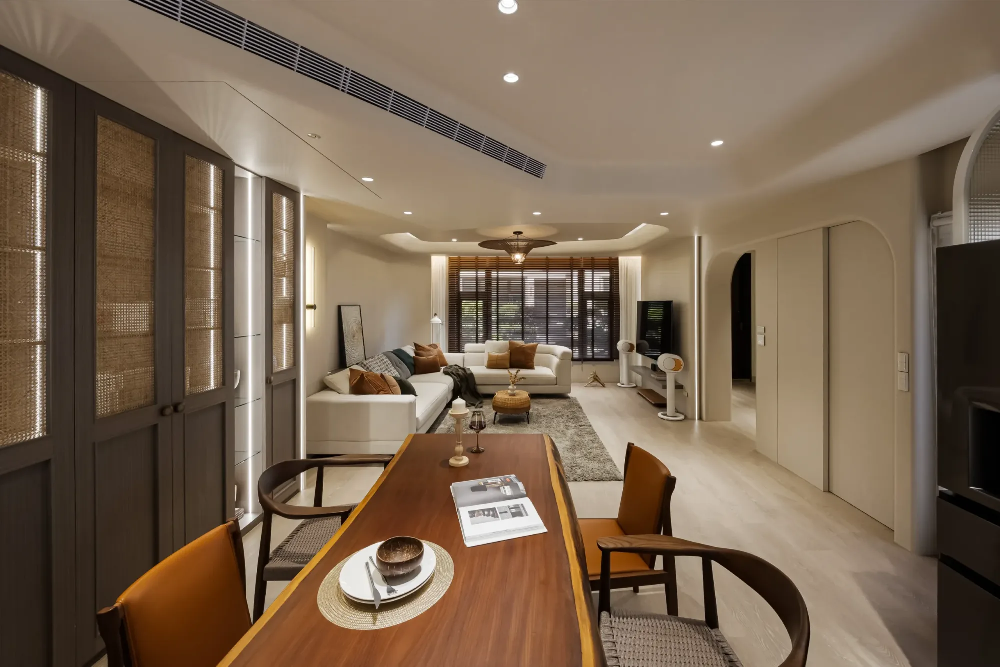 共構設計｜安興御松園 — 餐廳向客廳延伸廣角全景，奶油白色調搭配深木色餐桌、藤編櫃門與焦糖皮革單椅，嵌燈與間接燈光層次豐富｜空間攝影 / 琢磨影像