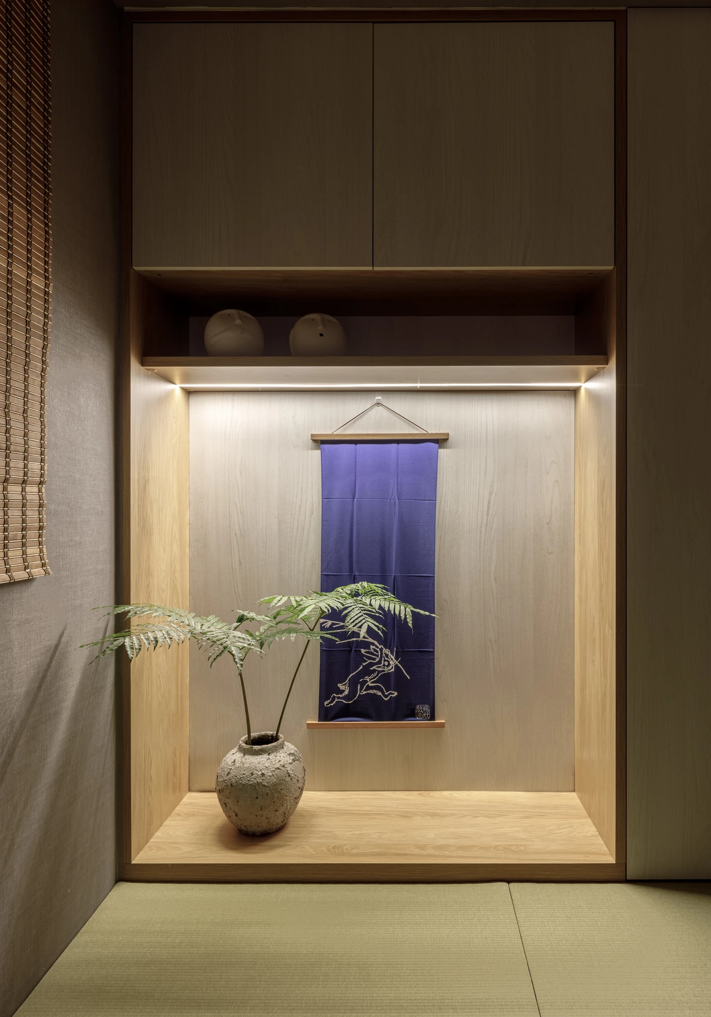 沐舍國際設計|惠宇朗庭 — 和室壁龕以淺木紋打造內嵌展示台,藍染掛軸與粗陶花器點綴其間,線型燈帶散發溫潤光暈,榻榻米與竹簾共同營造沉靜內斂的禪意氛圍|空間攝影 / 琢磨影像