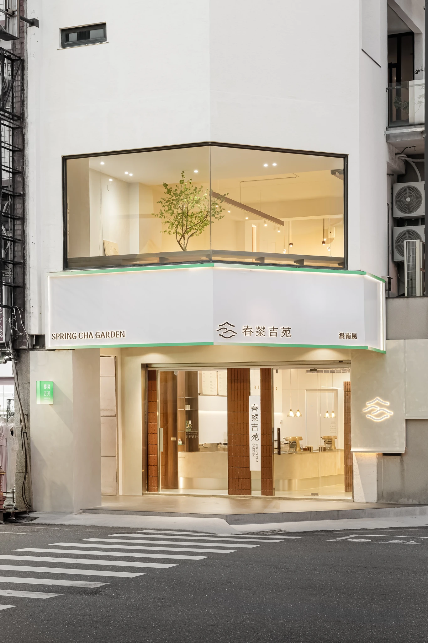 春茶吉苑 — 店面正向門面，白色發光招牌標示「春茶吉苑 SPRING CHA GARDEN」,紅磚門框與品牌標誌相襯，暮色中櫥窗暖光通透，呈現完整的商業門面設計｜空間攝影 / 琢磨影像