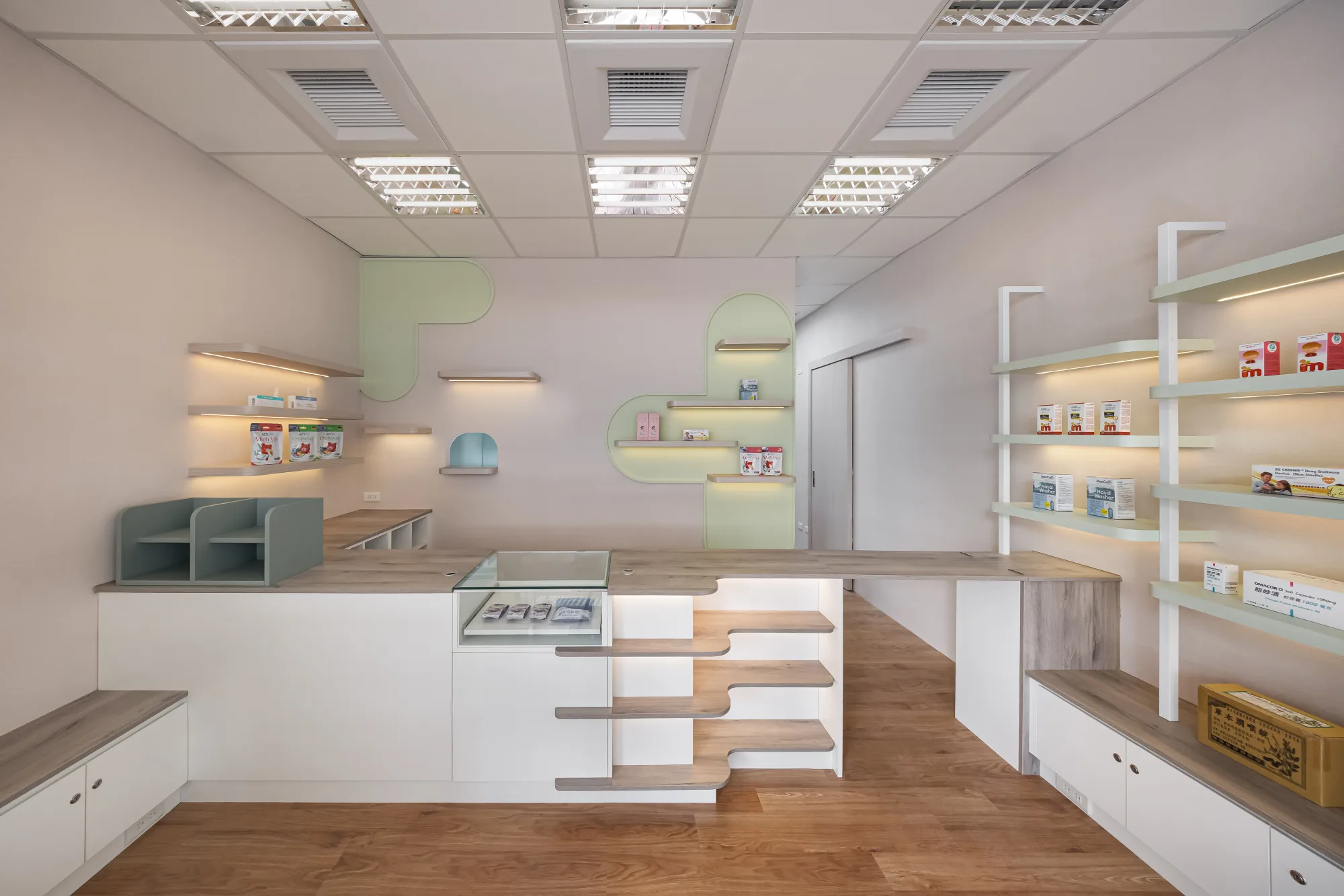 映墨設計|沐藥局 — 店內另一視角,白色結帳檯與薄荷綠層架、有機曲線木層板錯落陳列保健商品,後牆白色門片收整動線,呈現柔和的商業空間設計|空間攝影 / 琢磨影像