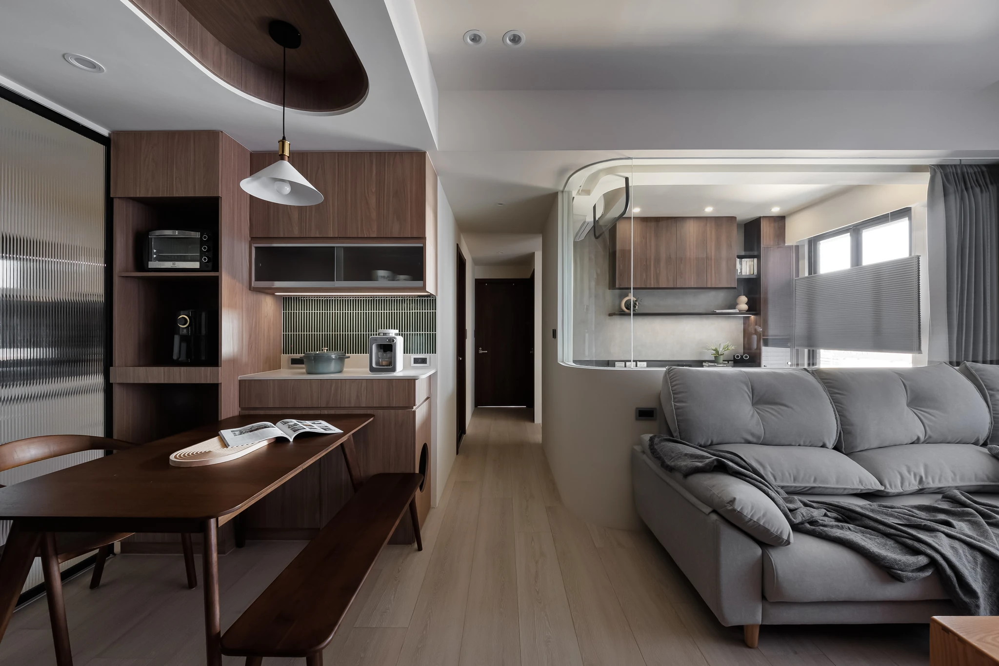 YJ Design|富宇富好 — 開放式餐廚望向客廳,胡桃木餐桌長凳與灰色沙發、弧形矮牆隔間|空間攝影 / 琢磨影像