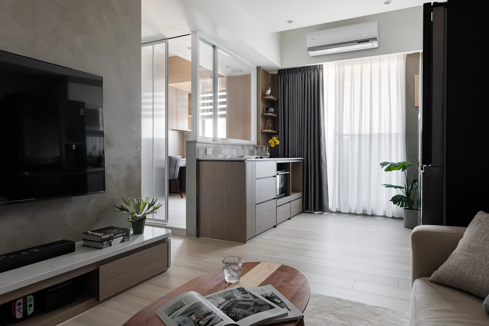 YJ Design｜陽光樹 — 客廳望向廚房玻璃隔間與陽台落地窗紗，灰泥電視牆與木地板｜空間攝影 / 琢磨影像